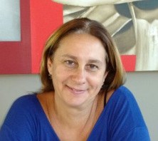 Professora Cristina Broglia Feitosa de Lacerda. Mulher parda, olhos castanhos, cabelo castanho, solto, liso e na altura dos ombros e solto. Ela usa roupa na cor azul e sorri.