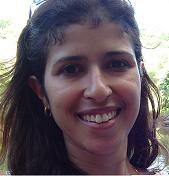 Professora Juliane Aparecida de Paula Perez Campos. Mulher parda, olhos castanhos, cabelo castanho, ondulado, solto e longo. Ela usa argola pequena dourada e sorri. 