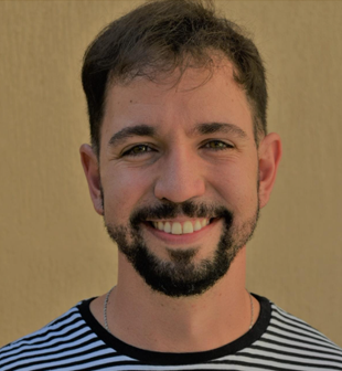 Professor Leonardo Santos Amâncio Cabral. Homem branco, olhos verdes, cabelo castanho, curto e liso. Ele está de frente para a foto, usa barba rente à pele, camiseta com listras horizontais pretas e brancas e sorri.